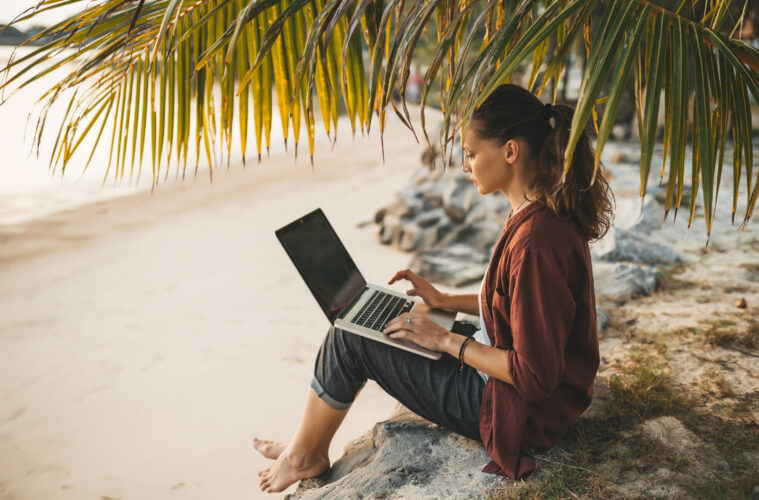 Woman sitting with laptop on the summer beach at sunset